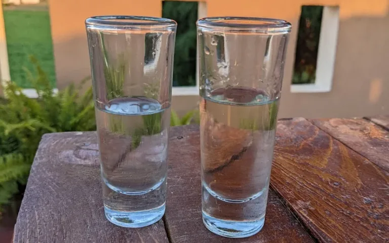 two shot glasses on outside table with clear liquid
